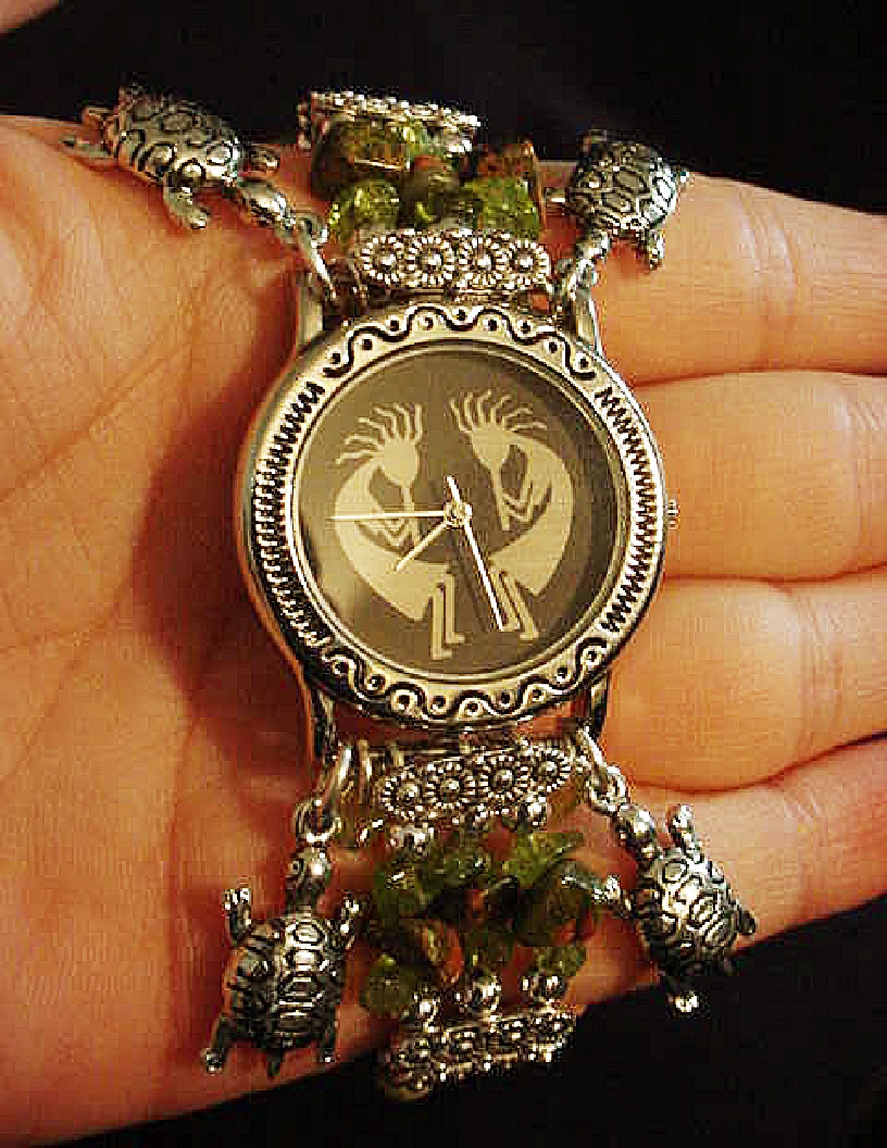 Handcrafted Semi-precious Kokopelli Watch 1- Handcrafted with Semi-precious Unachite and Peridot Stones. Embellished with Silver plated  beads and findings. Five turtle charms are used for final details. Stretch cord is used for watch bands. Round Large Silver watch face.
Two Kokopelli's designs enhance the watch sphere. Quartz function and mechanical system. Stainless Steel back.Beautiful, Elegant and Southern look.