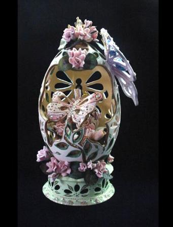 This flowery carved eggypiece is painted in matte light peach and green enamel details. Top clay butterfly shape cut front, hand crafted separately. Inside, a hand crafted butterfly painted in pastel colors and gold enamel w/glitter and Austrian Crystals details. Resting on a bunch of porcelain roses in pastels colors. Clay stand w/gold and glitter finish. AB crystals and beads used for final details. Decorated box available for this eggypiece.