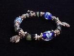 Handcrafted Jewelry Blue & Green Glass Beads Bracelet - Handcrafted with Blue Glass and Green Semi-precious stones beads. Transparent Lampwork White and Blue  flower glass beads are used for a floral and romantic look. Embellished with Silver plated  beads, charms and findings. Stretch cord is used for flexibility.  Beautiful and Elegant!