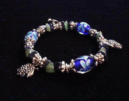 Handcrafted Jewelry Blue & Green Glass Beads Bracelet - Handcrafted with Blue Glass and Green Semi-precious stones beads. Transparent Lampwork White and Blue  flower glass beads are used for a floral and romantic look. Embellished with Silver plated  beads, charms and findings. Stretch cord is used for flexibility.  Beautiful and Elegant!